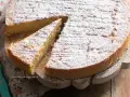 Una deliziosa torta di riso, cosparsa di zucchero a velo, su un tagliere di legno. Una fetta è già stata servita.