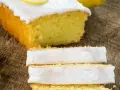 Fetta di plumcake al limone con glassa bianca e una fetta di limone sopra, su un tagliere di legno.