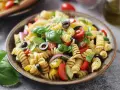 Pasta fredda con pomodorini, olive, basilico e cipolla rossa. Un'idea fresca e gustosa su cosa mettere nella pasta fredda per un pranzo estivo.