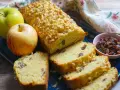 Plumcake alle mele dorato, con pinoli e uvetta, accompagnato da mele fresche e una ciotolina di uvetta.