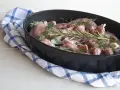 Pezzi di coniglio crudo pronti per essere cucinati al forno, profumati con rosmarino, salvia e aglio.
