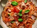 Spaghetti al sugo di pomodoro con abbondante tonno in scatola, guarniti con foglie di basilico fresco. Un piatto semplice e gustoso.