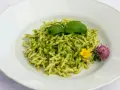 Un piatto di trofie al pesto, guarnito con basilico fresco e fiori di campo, pronto per essere gustato.