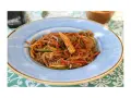 Un piatto di spaghetti di riso con verdure colorate, tra cui peperoni, carote e pannocchiette, condito con una salsa saporita.