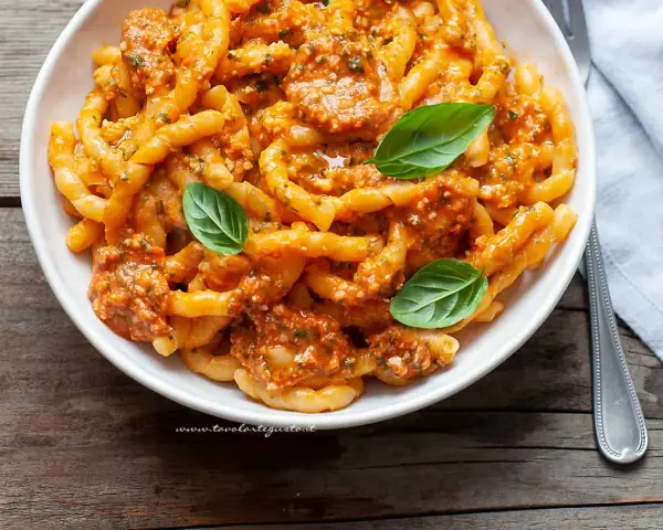 Un piatto invitante di busiate alla trapanese, condite con un sugo rosso e guarnite con foglie di basilico fresco.