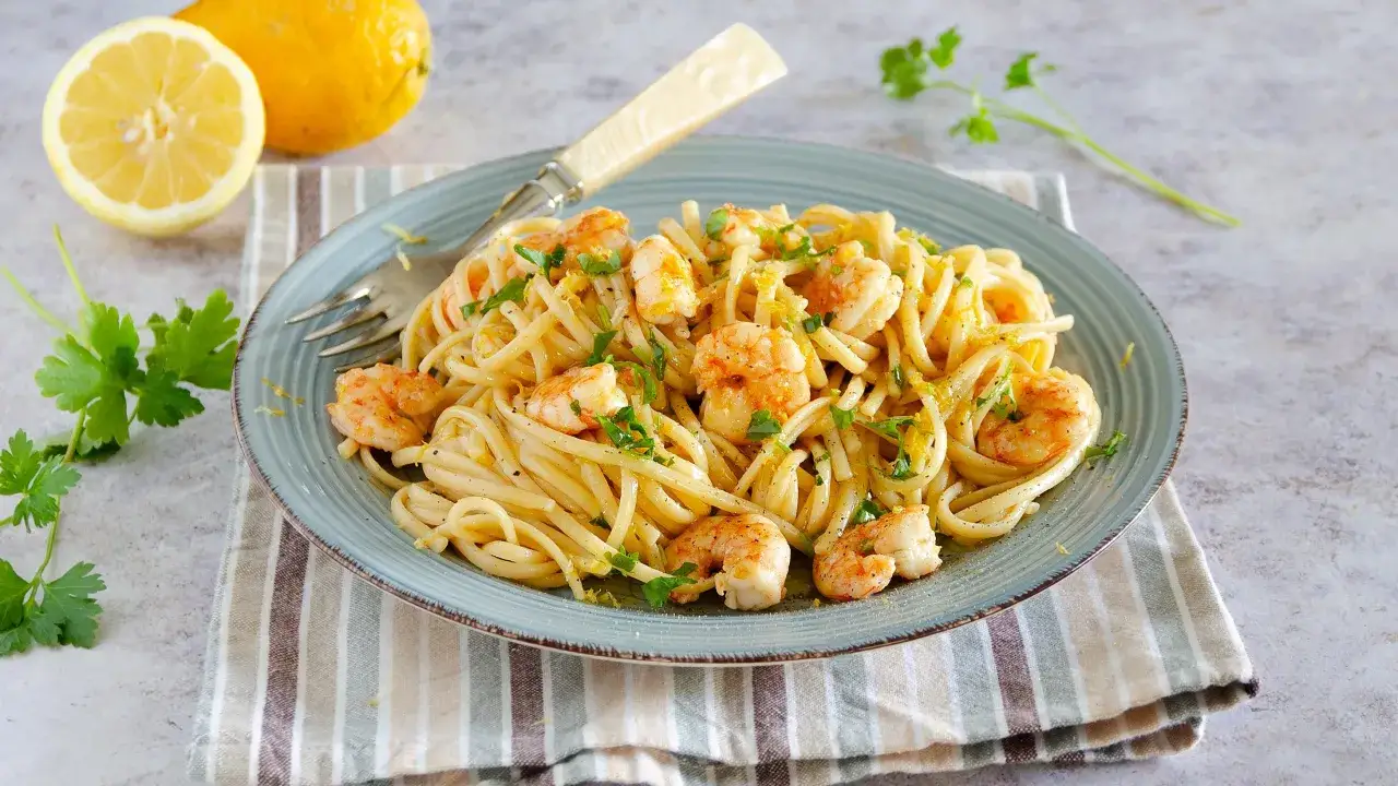 Un piatto di pasta con gamberetti, condita con limone e prezzemolo, accompagnata da limoni freschi e parmigiano.