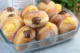 Bomboloni ricetta originale ripieni di crema e cioccolato, cosparsi di zucchero. Un dolce invitante pronto da gustare.