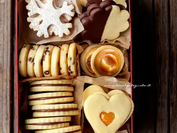 Scatola piena di biscotti al burro: fiocchi di neve, con gocce di cioccolato, ripieni di caramello e a forma di cuore.