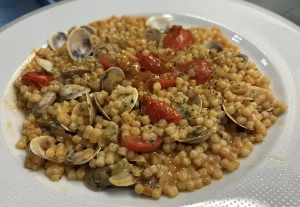 Un piatto invitante di fregola con vongole, pomodorini e prezzemolo, pronto per essere gustato.