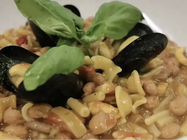 Un piatto invitante di pasta fagioli e cozze, guarnito con foglie di basilico fresco.