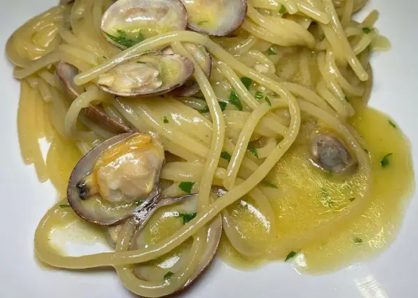 Spaghetti alle vongole cremosi come al ristorante, con vongole fresche e prezzemolo tritato su un letto di pasta dorata.