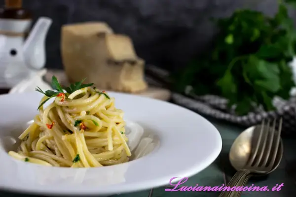Un piatto di spaghetti alla carrettiera, conditi con aglio, olio, peperoncino e prezzemolo, con pecorino grattugiato sullo sfondo.