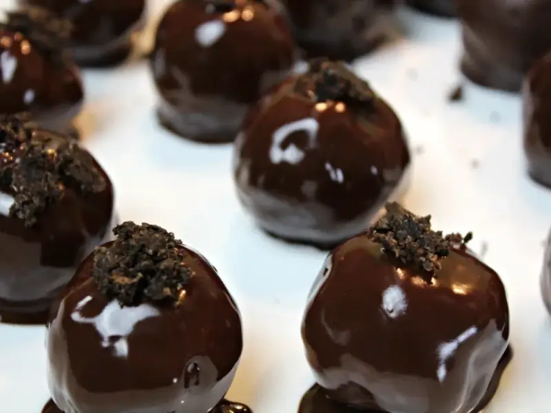 Deliziosi tartufini al cocco ricoperti di cioccolato fondente lucido, guarniti con briciole croccanti.